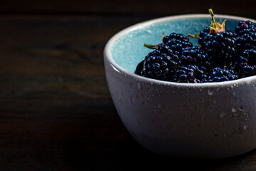 Ripe blackberries with leaves in a clay bowl on a  wooden background dark food photography, Sweet tasty heap Antioxidant organic superfood