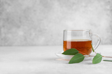 Cup of fresh black tea with green leaves on gray background.