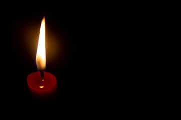 Red candle with yellow flame on black background
