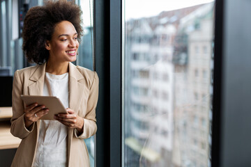 Happy business woman manager holding tablet and working in modern office