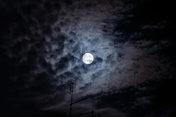 Full moon at night. The illuminated face of the moon is wrapped in a cloud cover that covers it in...