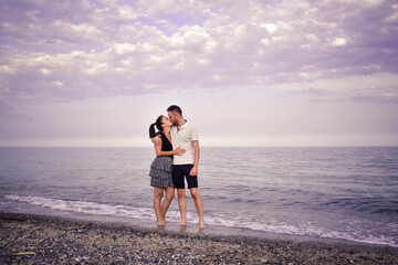 Fototapeta na wymiar Pareja besandose en la orilla de la playa frente al mar, con un cielo repleto de nubes