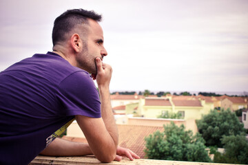 Chico apoyado en un balcón pensativo mirando el paisaje