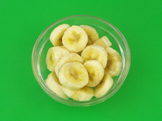 Banana slices in glass bowl on green background