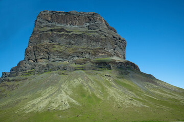 großer massiver Felsen auf einem grünen Berg vor blauem Himmel
