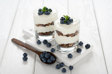 Dessert with cottage cheese, fresh blueberries and granola in a glass on a white wooden background.