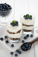 Dessert with cottage cheese, fresh blueberries and granola in a glass on a white wooden background.