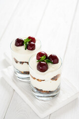 Dessert with cheese, fresh cherries and granola in a glass on a white wooden background.