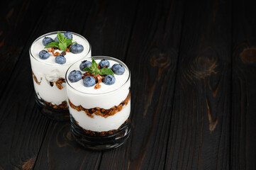 Homemade layered dessert with fresh blueberries, cream cheese or yogurt, granola on rustic background.