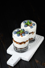 Homemade layered dessert with fresh blueberries, cream cheese or yogurt, granola on rustic background.