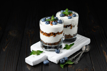 Homemade layered dessert with fresh blueberries, cream cheese or yogurt, granola on rustic background.