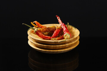 Dried peppers on a stack of wooden plates on a dark table with reflection. Close-up