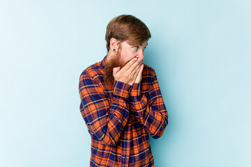 Young caucasian red-haired man isolated on blue background laughing about something, covering mouth with hands.