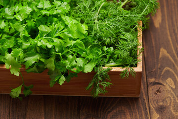 a top of bunch of green dill, parsley, salad, herbs and other greens in a wooden box, dark wood background, concept of fresh vegetables and healthy food