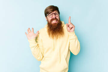 Fototapeta premium Young caucasian red-haired man isolated on blue background holding and showing a product on hand.