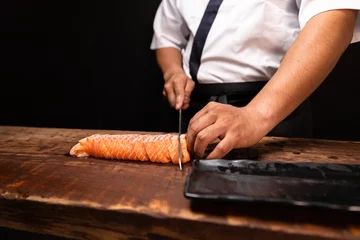 Selbstklebende Fototapeten Chef's hand holding fresh piece of salmon.Closeup of chef hands preparing japanese food. Japanese chef making sushi at restaurant.Chef making traditional japanese sushi on wood board. © anon