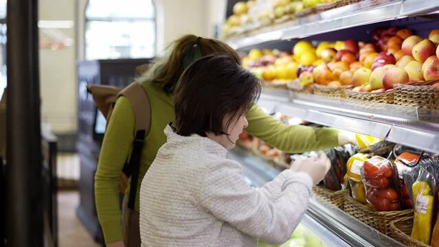 Down syndrome girl with her mother taking vegetables from shelf in supermarket