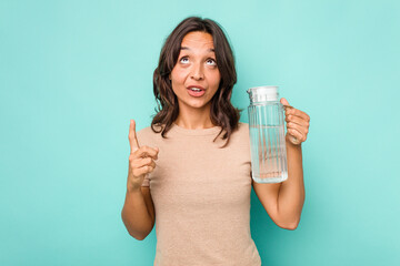 Young hispanic woman holding a water of jar isolated on blue background pointing upside with opened mouth.