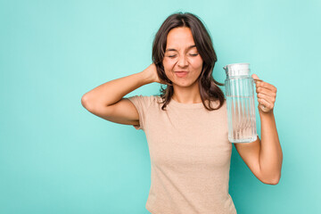 Young hispanic woman holding a water of jar isolated on blue background touching back of head,...