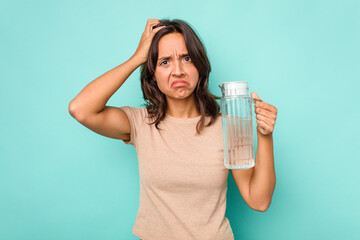 Young hispanic woman holding a water of jar isolated on blue background being shocked, she has remembered important meeting.