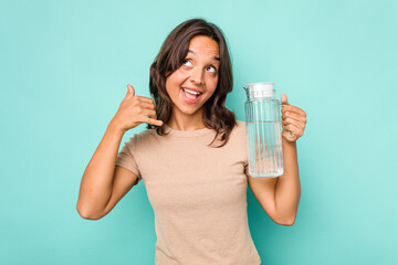 Young hispanic woman holding a water of jar isolated on blue background showing a mobile phone call gesture with fingers.
