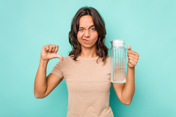 Young hispanic woman holding a water of jar isolated on blue background showing a dislike gesture, thumbs down. Disagreement concept.