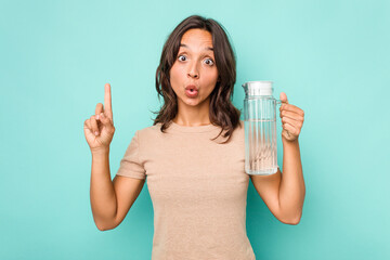 Young hispanic woman holding a water of jar isolated on blue background having some great idea,...