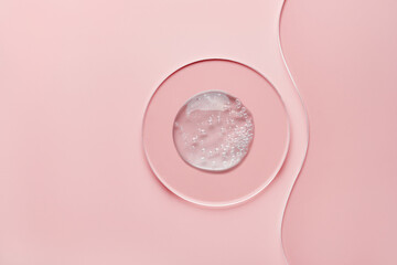 Round petri dish with gel cosmetic product and wavy glass slide on pink background