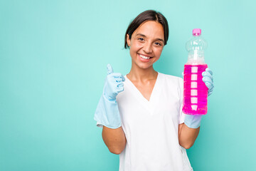 Young cleaner hispanic woman isolated on blue background smiling and raising thumb up