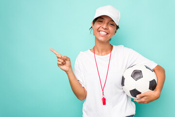 Young hispanic soccer referee woman isolated on blue background smiling and pointing aside, showing...