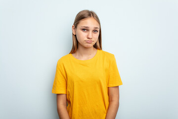 Young caucasian girl isolated on blue background blows cheeks, has tired expression. Facial expression concept.