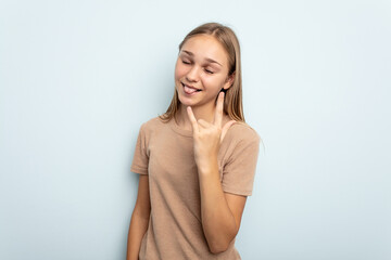 Fototapeta premium Young caucasian girl isolated on blue background showing rock gesture with fingers