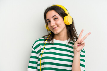 Young caucasian woman listening to music isolated on white background joyful and carefree showing a peace symbol with fingers.