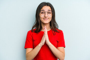Fototapeta premium Young caucasian woman isolated on blue background holding hands in pray near mouth, feels confident.