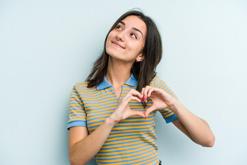 Young caucasian woman isolated on blue background smiling and showing a heart shape with hands.