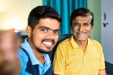 Happy smiling son with father making vlogs or on video call at home - concept of influencer, social video making and relationship bonding.