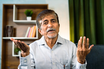 Confident elderly senior man talking by looking camera at home on video call - concept of expert advice, inspiration and intellect.