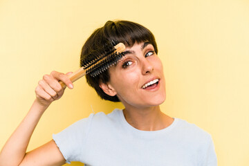 Obraz premium Young caucasian woman holding a brush hair isolated on yellow background