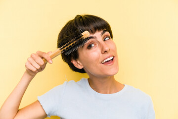 Young caucasian woman holding a brush hair isolated on yellow background