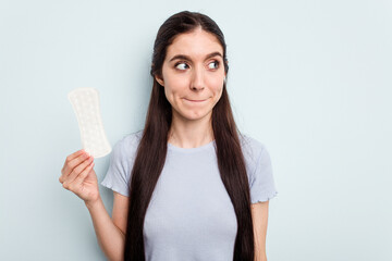 Young caucasian woman holding a sanitary napkin isolated on blue background confused, feels doubtful and unsure.