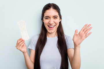 Young caucasian woman holding a sanitary napkin isolated on blue background receiving a pleasant surprise, excited and raising hands.