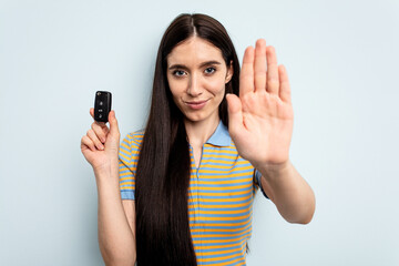 Fototapeta premium Young caucasian woman holding car keys isolated on blue background standing with outstretched hand showing stop sign, preventing you.