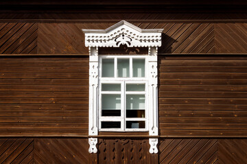 carved window in Russian old style with white architraves, on wooden background