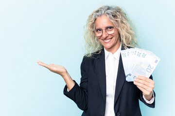 Middle age business caucasian woman holding bank notes isolated on white background showing a copy space on a palm and holding another hand on waist.