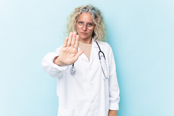 Middle age caucasian woman isolated on blue background standing with outstretched hand showing stop...