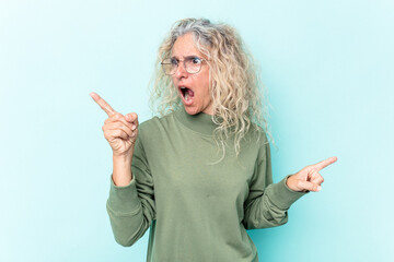 Middle age caucasian woman isolated on blue background pointing to different copy spaces, choosing one of them, showing with finger.