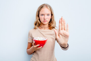 Caucasian teen girl eating cereals isolated on blue background standing with outstretched hand showing stop sign, preventing you.