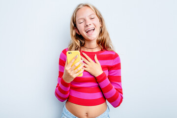 Caucasian teen girl holding mobile phone isolated on blue background laughs out loudly keeping hand on chest.