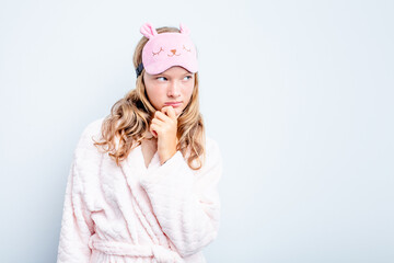 Caucasian teen girl wearing a pajama isolated on blue background looking sideways with doubtful and skeptical expression.