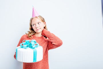 Caucasian teen girl holding a cake isolated on blue background touching back of head, thinking and making a choice.